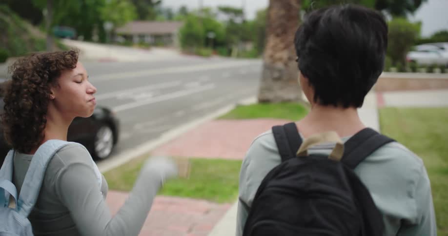 Two teenagers with backpacks walking along the sidewalk of an urban street