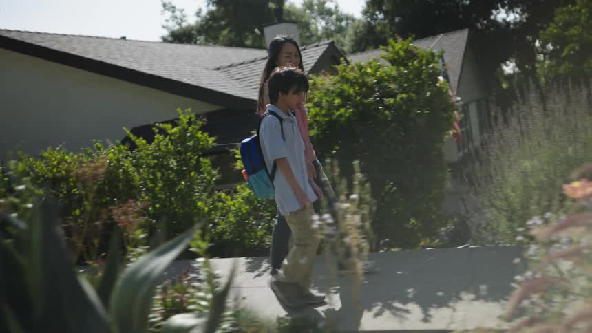Mother and son walk along a residential sidewalk passing a flower garden