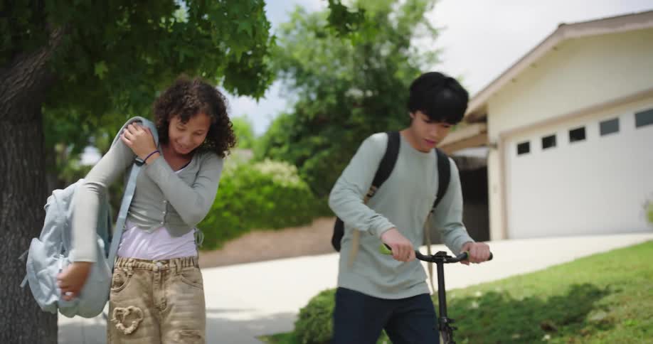 Boy helping a girl stand up and they ride a scooter down the sidewalk