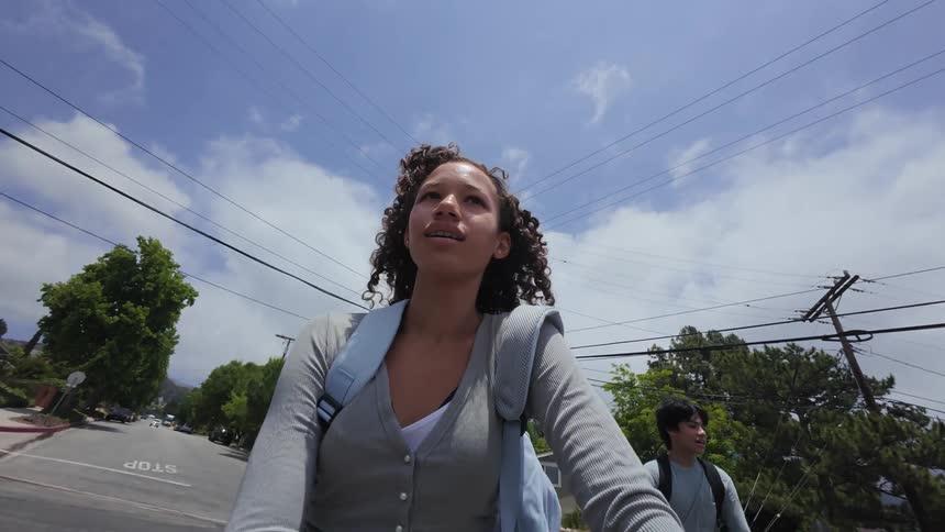 Curly haired girl walking on an urban street accompanied by a boy behind her