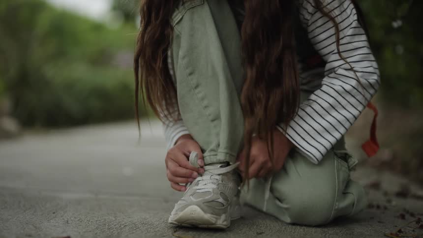 Girl half kneels on the sidewalk while tying her shoe during the daytime