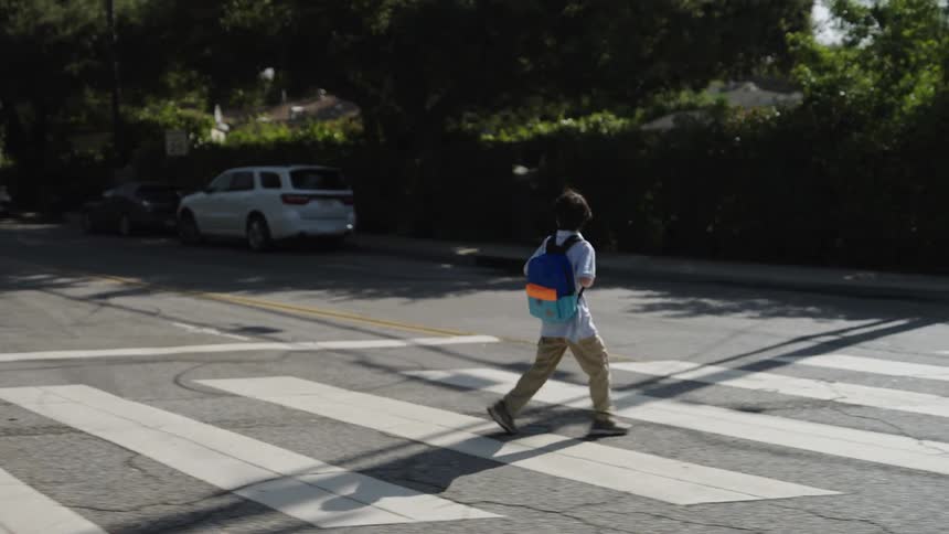 Youth wearing a backpack walks across a crosswalk on a sunny day