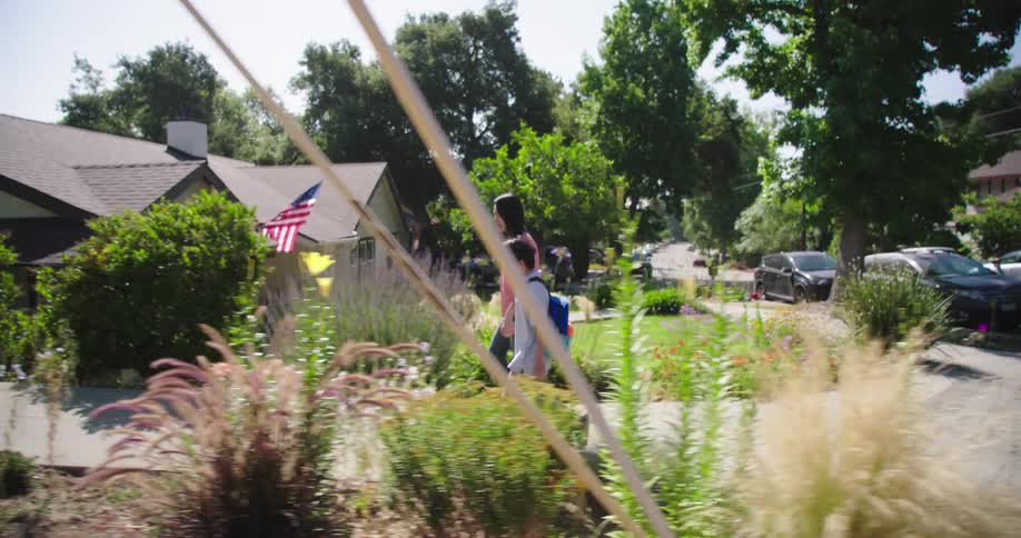 A teenager is walking a child home from school on the sidewalk at midday