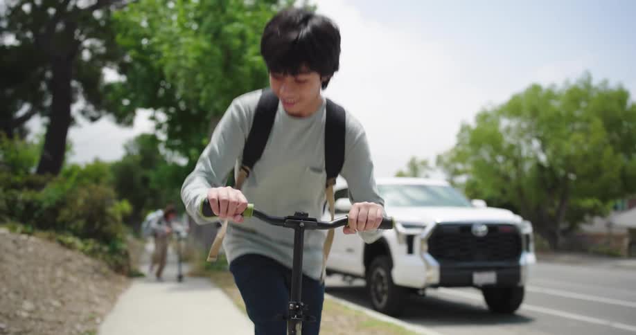 Two teenagers riding scooters on a suburban sidewalk