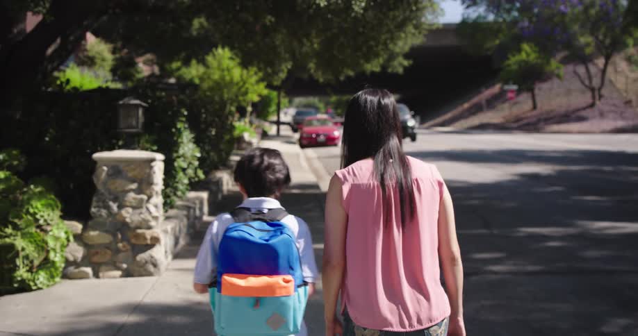 Mother walking with a child on the sidewalk next to an urban road