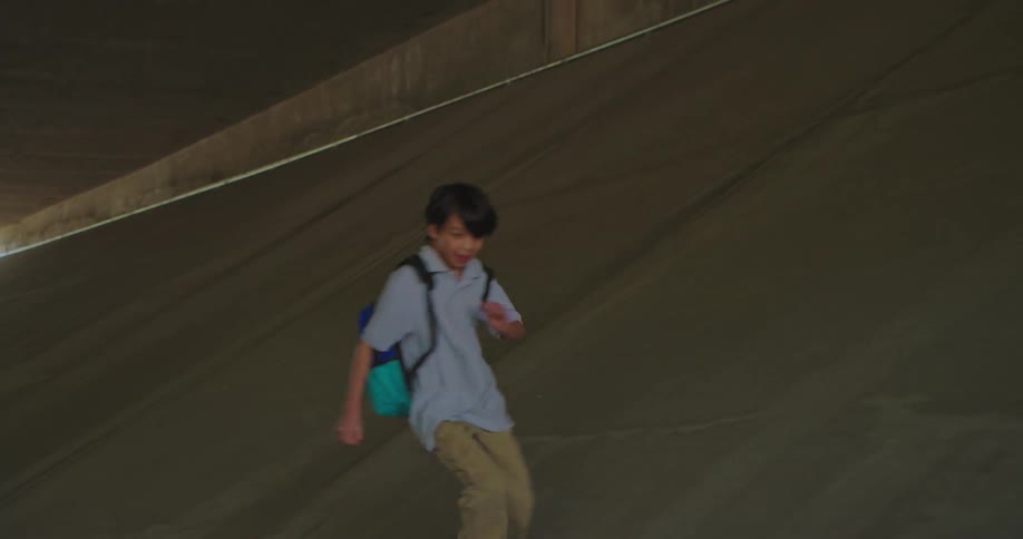 A young boy is running on the pavement beside a teenage girl as they walk along the side of the road at midday