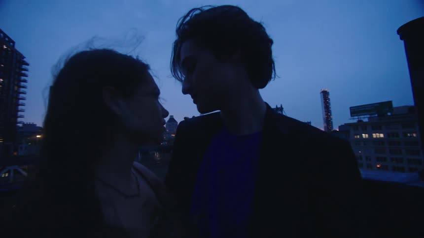 A couple hold hands and gaze at each other on the roof