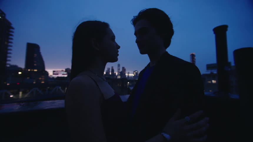 A couple gazes into each others eyes romantically on a rooftop at dusk