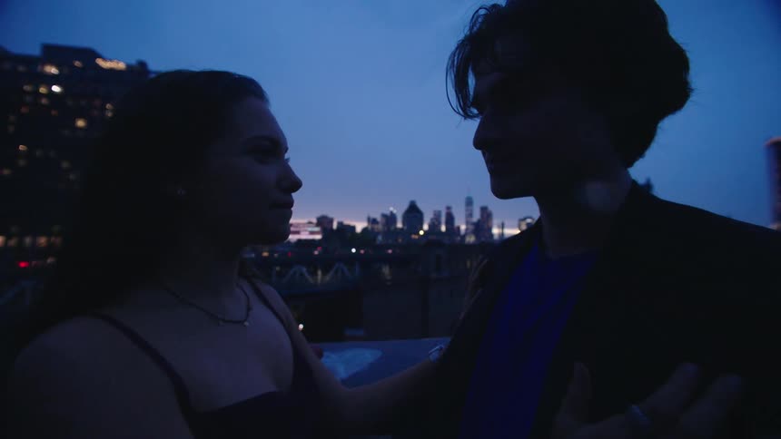 A man and woman kiss on the roof top at sunset