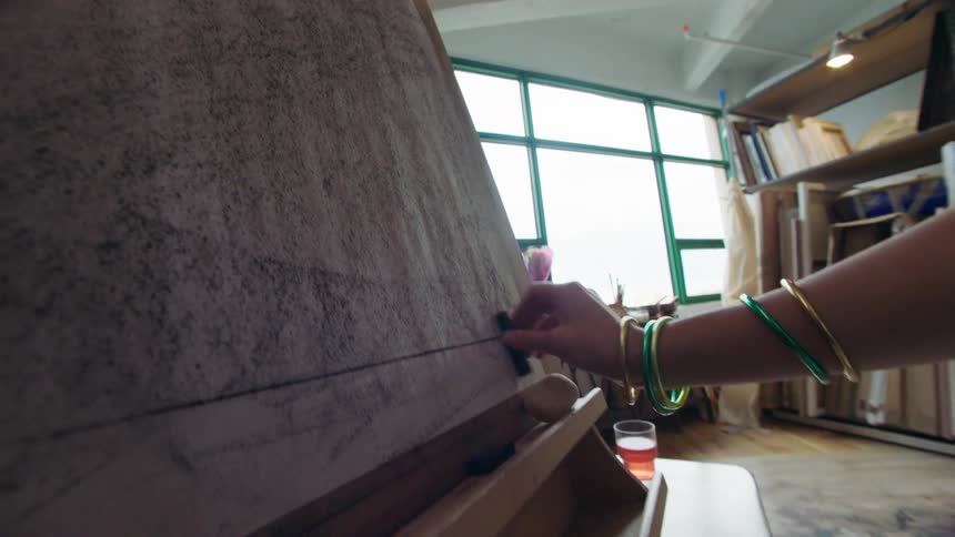 The woman is using charcoal on the canvas