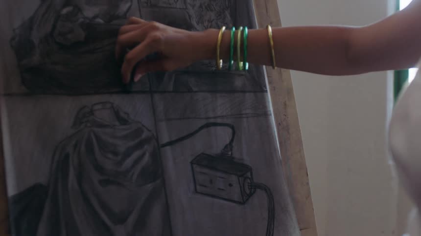 A person wearing green bangles sketches a detailed scene on a large sheet of paper
