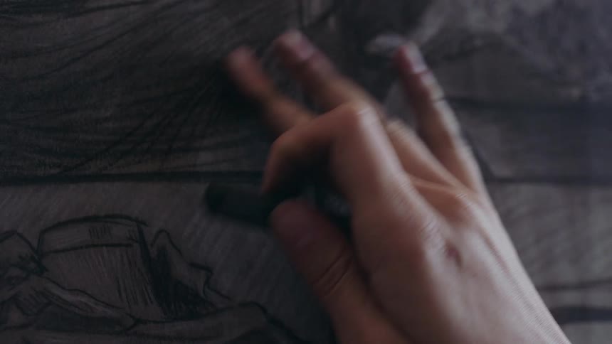 A hand using charcoal to add detail to a drawing on a canvas