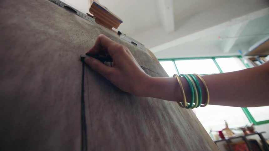 A hand with stacked bracelets applying charcoal to a large drawing