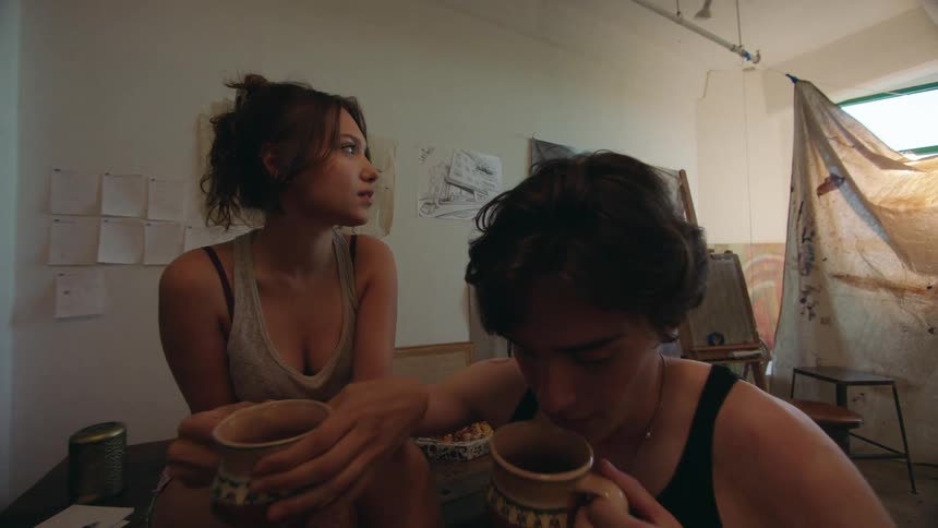 A young couple shares a quiet moment in a cozy artfilled studio space with drawings pinned to the walls