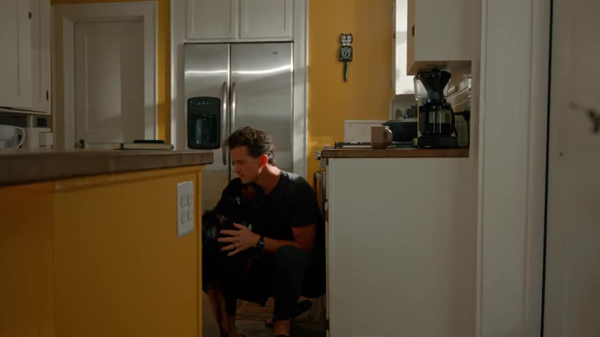 Young man pets and kisses his dog indoors in a kitchen during daytime