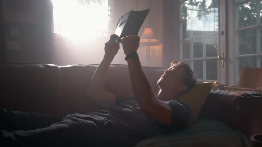 A man lays on his couch reading his notebook