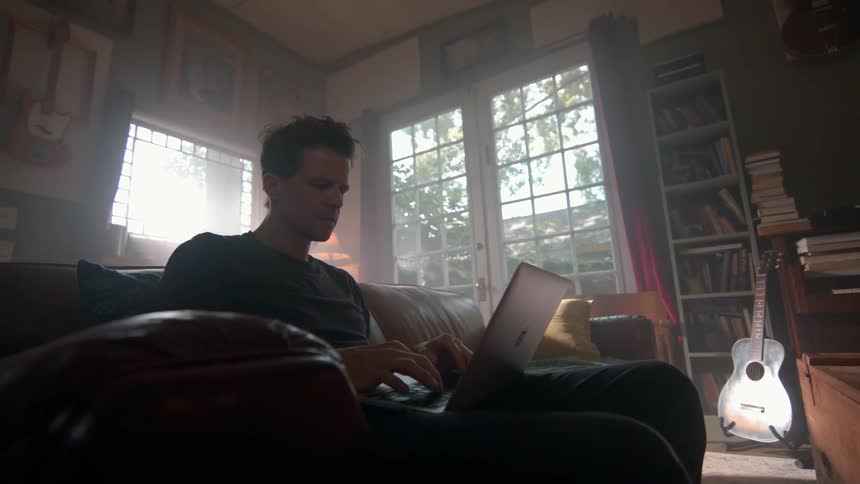 Man sitting on a sofa in the living room typing on a laptop