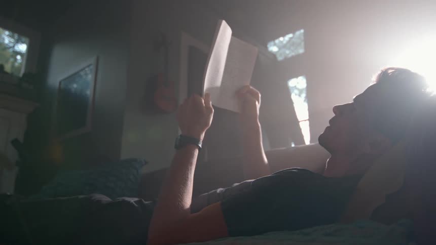 A man reads a book while lying down on a couch in a living room during daytime