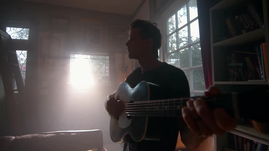 The man is playing the guitar by the window