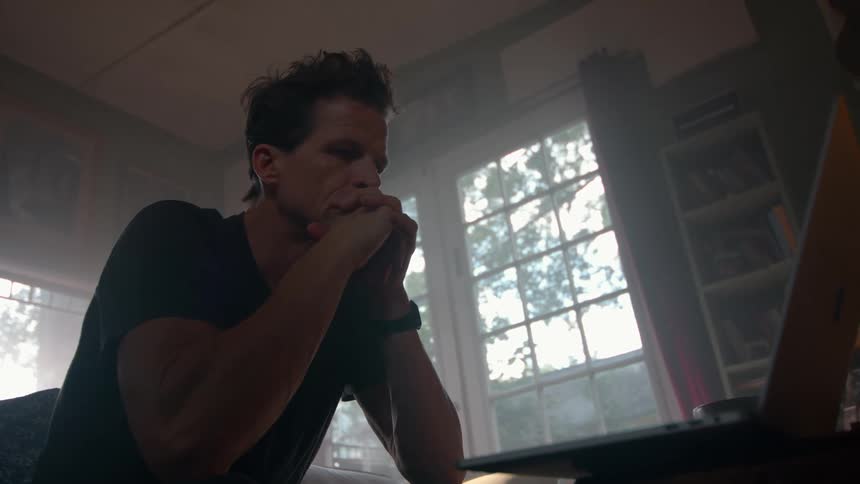 A man sits in a living room typing fast on a laptop computer