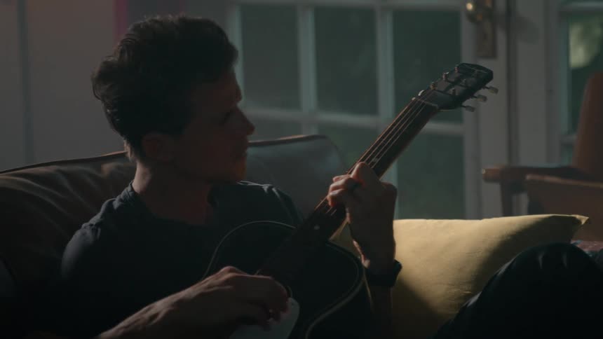 A man sits to strum on the guitar on the couch