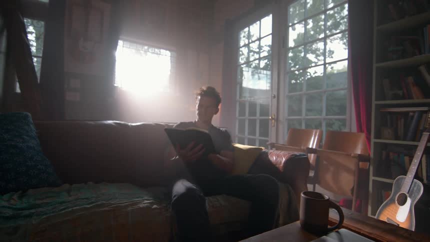 A man sits on the couch and reads a book