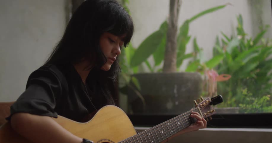 The woman is playing the guitar in front of a laptop