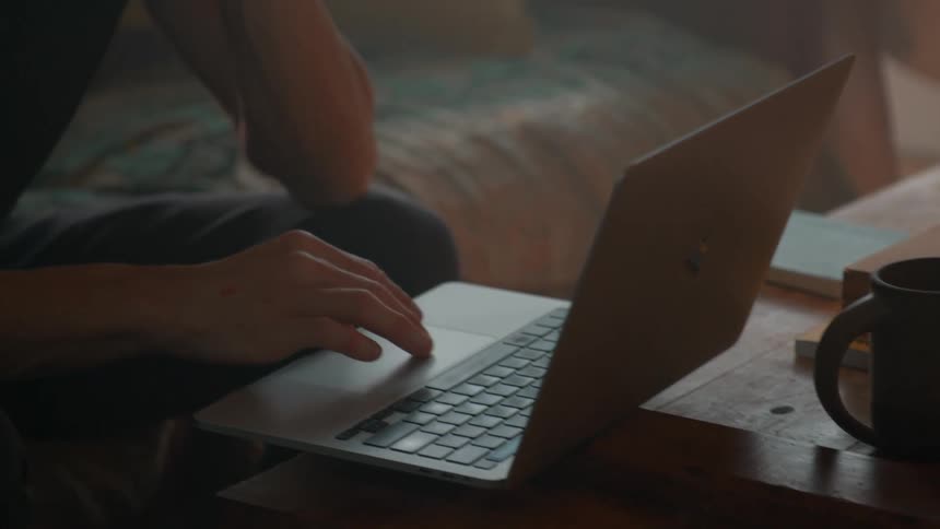 A young man is in his bedroom typing on his laptop