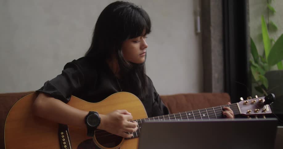Female sitting on couch strumming an acoustic guitar