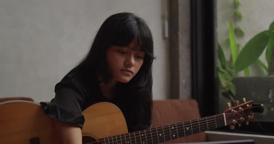 Young woman holding a guitar and typing in a laptop