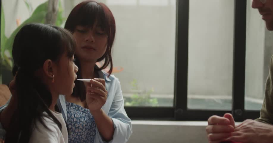 A girl is having her temperature taken by her mother while a doctor observes in a medical office