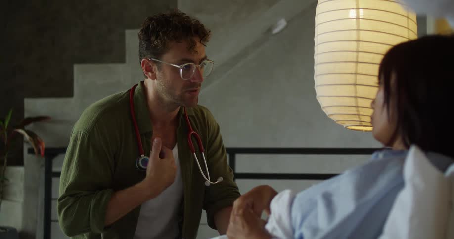 A doctor with a stethoscope gestures empathetically while speaking to a patient in a contemporary softly lit room