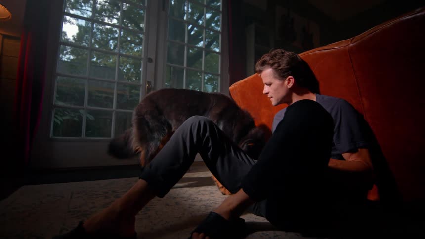 Man sitting in living room and playing with dog