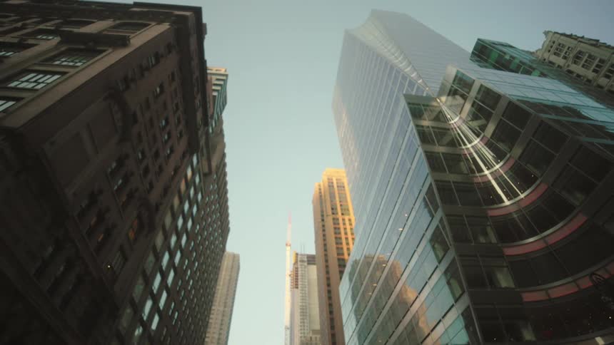 Tall city buildings rise against a clear sky as evening light touches their facades