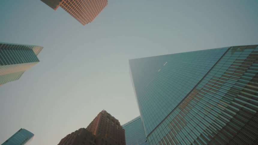 Multiple modern highrises with varied facades stretch skyward under soft daylight viewed from a low angle
