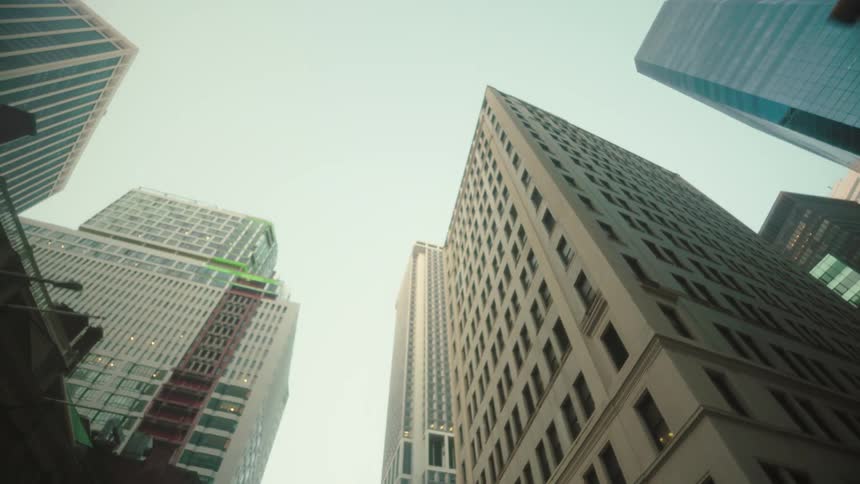 Skyscrapers tower upward from a low angle with rows of windows forming sharp vertical lines against the bright sky