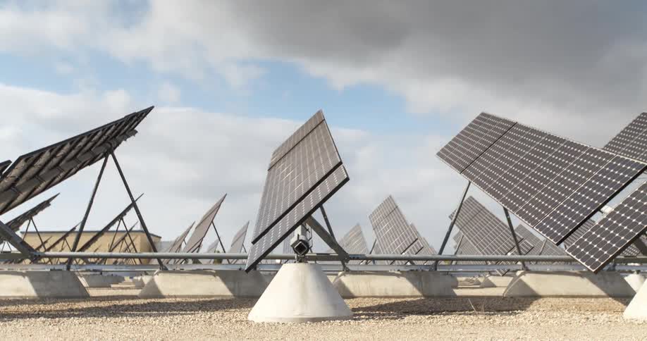 Several solar panels facing upwards in an outdoor environment with clouds passing quickly in the sky