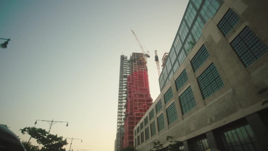 A wide angle view from below shows a large red building under construction with exposed rebar and scaffolding all against a bright clear sky