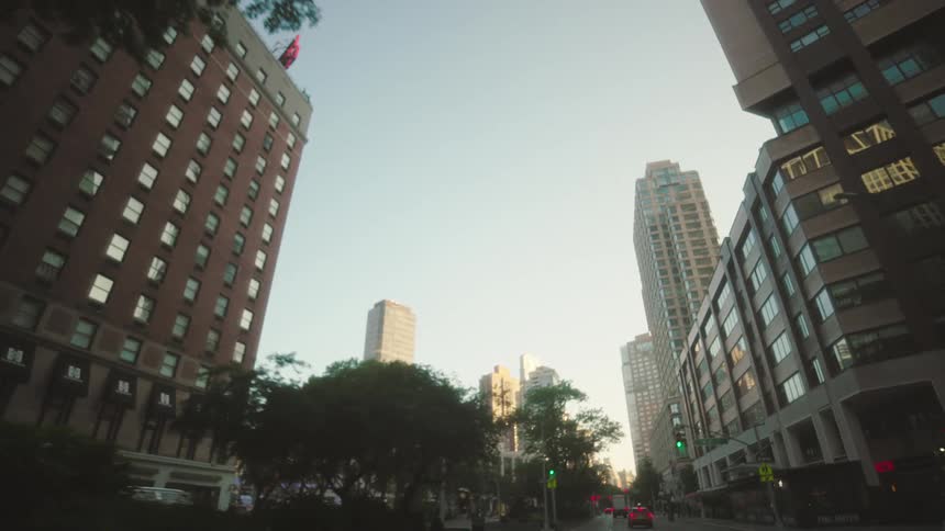 Cars drive by the tall buildings and pass the traffic lights