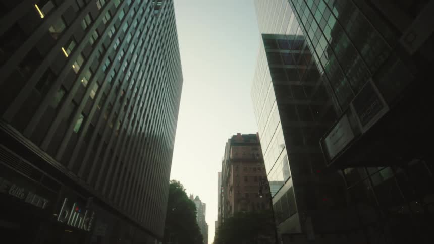 Several tall city buildings with numerous windows line a street creating a narrow view of a bright clear sky above