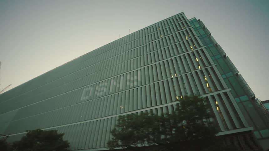 A tall modern building with a large advertising banner on its side stands prominently on a city street with buildings under construction in the background