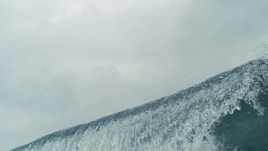 A powerful ocean wave crests under a cloudy sky