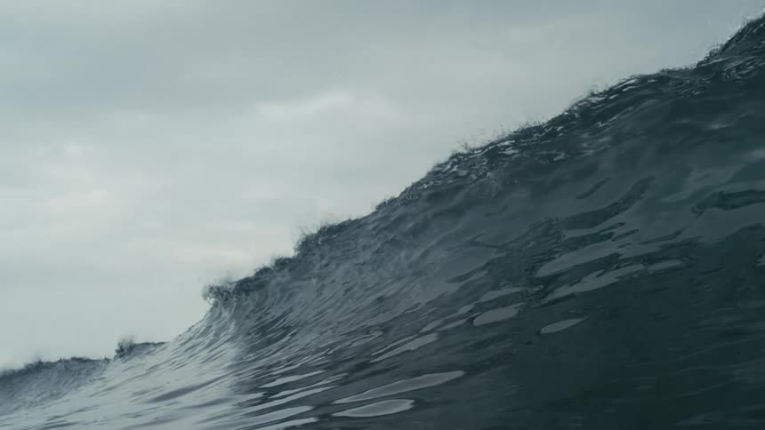 Wave forming and breaking in the ocean against a cloudy sky