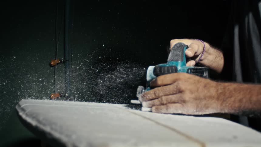 A worker uses a power tool to sand a surface sending particles flying in a dark workspace