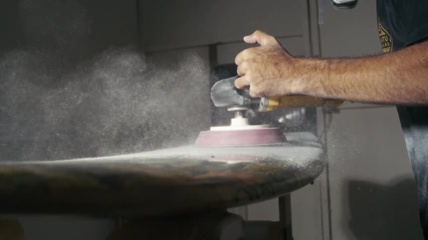 Person using an electric sander to make a surfboard