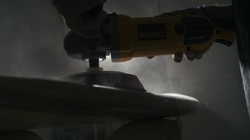 Pair of hands using an electric sander on a surfboard
