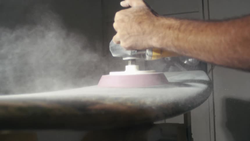 Hands on an electric sander on a surfboard