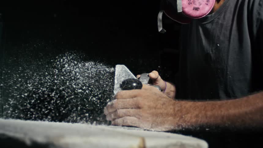 Man in mask sanding a surfboard