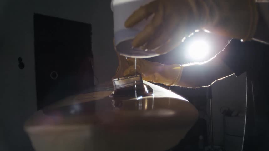 Pair of gloved hands pouring resin liquid onto the surface of a surfboard