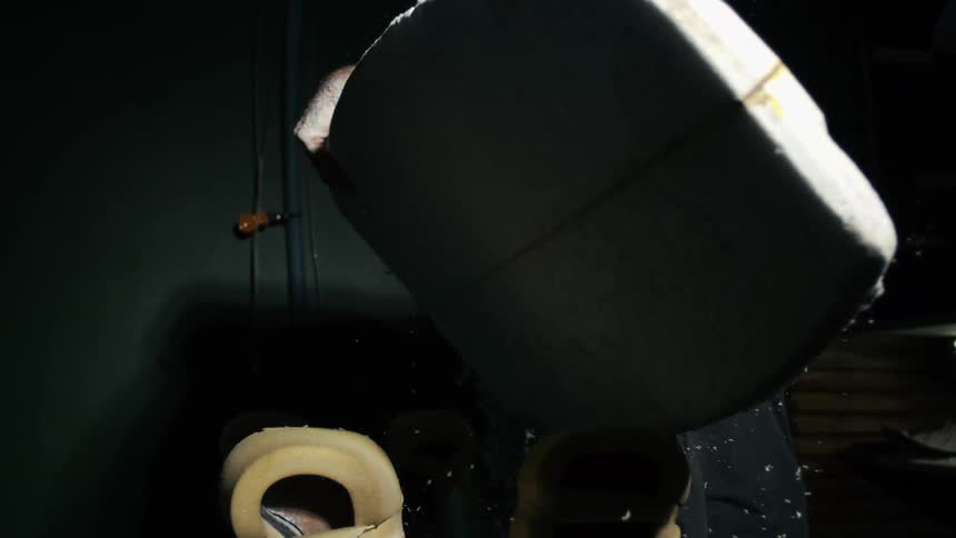 A man shapes a large board under focused light in a dim workshop